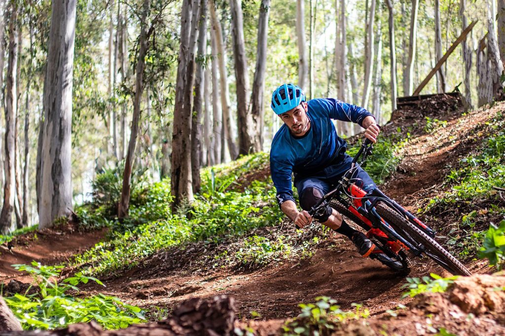 Mountainbiker in blauem Outfit fährt durch einen Wald auf einem schmalen Pfad.