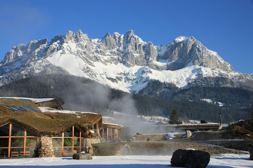 Berglandschaft des Wilden Kaiser mit Therme bei Going zum Baden im Vordergrund, umgeben von majestätischen Gipfeln und klarem blauen Himmel.